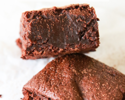 A fudgey chocolate brownie leans against another brownie. The brownies sit on a white piece of parchment paper and are sprinkled with cocoa powder. Text overlay reads "super fudgey oat flour brownies."