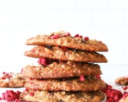 This is a side view of a stack of cookies. The stack sits on a white piece of parchment paper and a white background. Freeze dried raspberries are around the cookies.