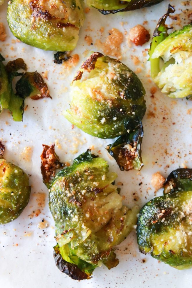 This is an overhead image of brussels sprouts on a piece of parchment paper. The roasted brussels are crispy and have golden parmesan on it.