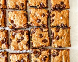 This is an overhead image of 16 banana chocolate chip blondie bars on a white piece of parchment paper.