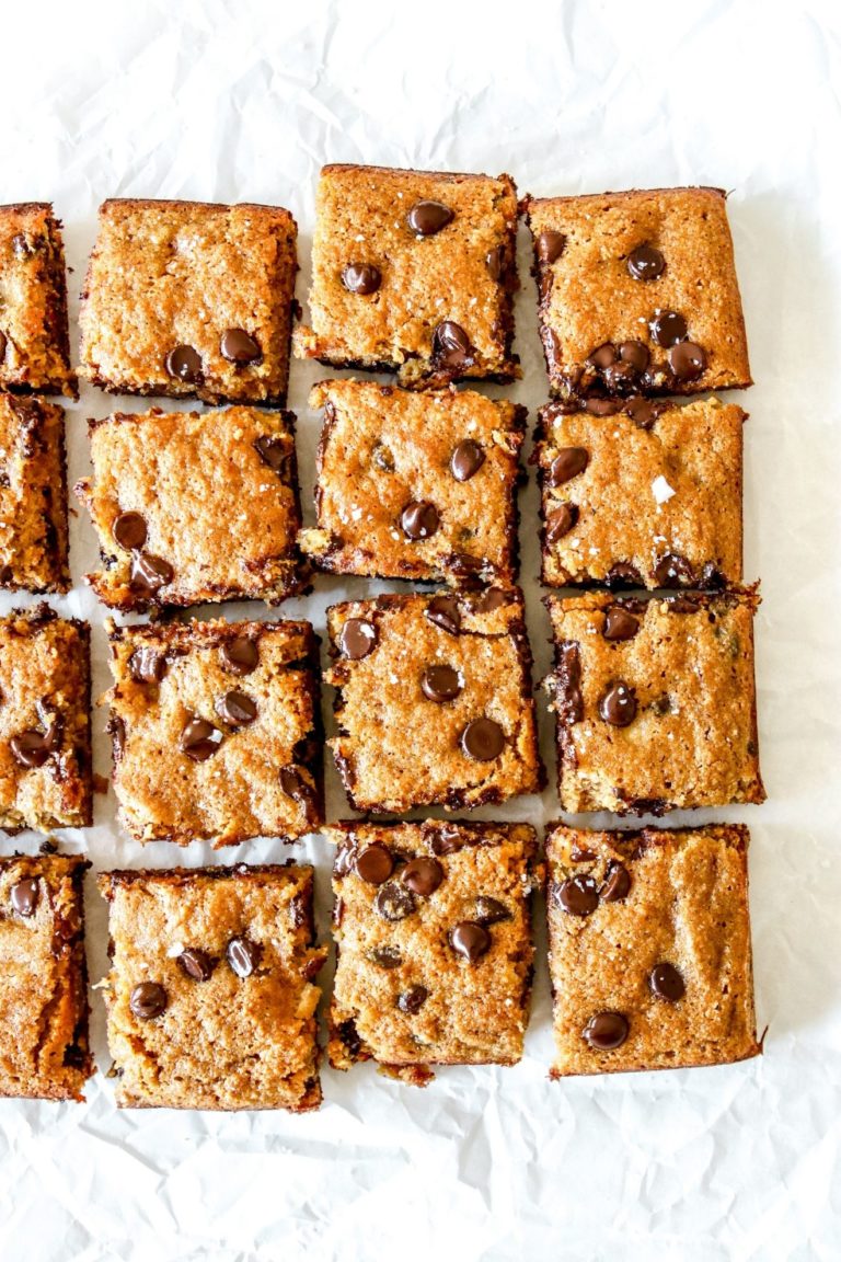 This is an overhead image of 16 banana chocolate chip blondie bars on a white piece of parchment paper.