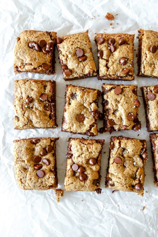 This is an overhead image of 12 tahini bars with chocolate chips. The bars sit on a wrinkled piece of white parchment paper.