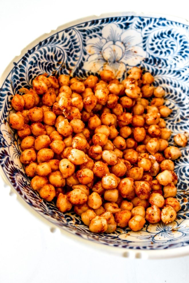 This is a side view of a blue and white bowl on a white counter. Inside the bowl is chickpeas coated with spices.