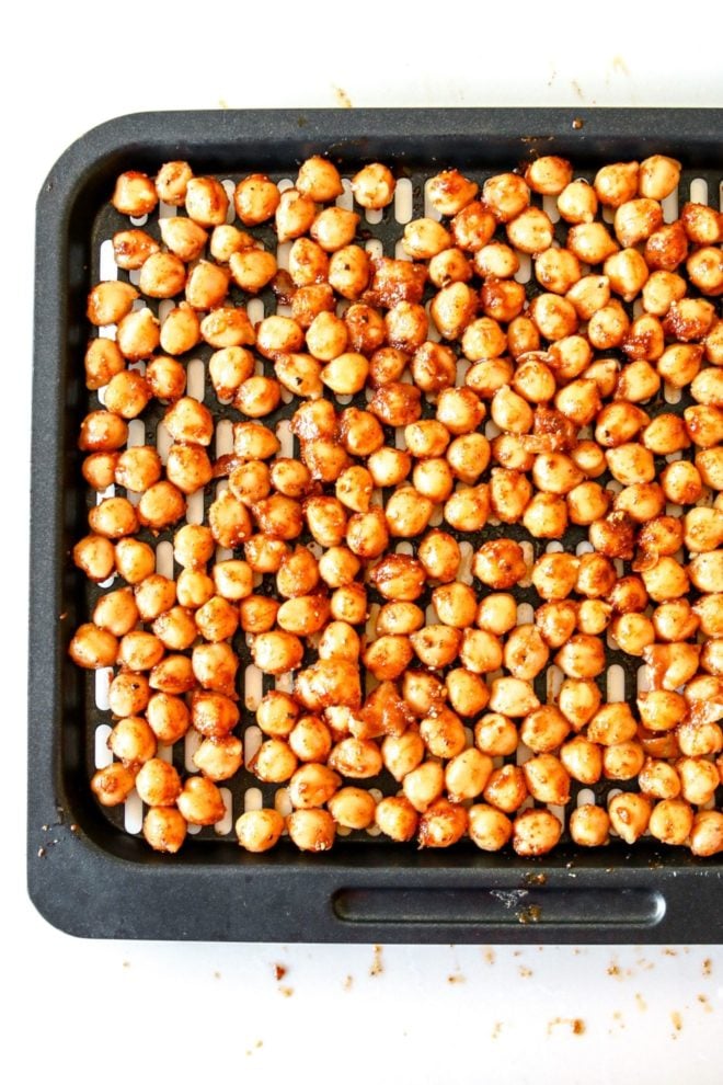 This is an overhead view of an air fryer tray with chickpeas coated with spices. The tray sits on a white counter.