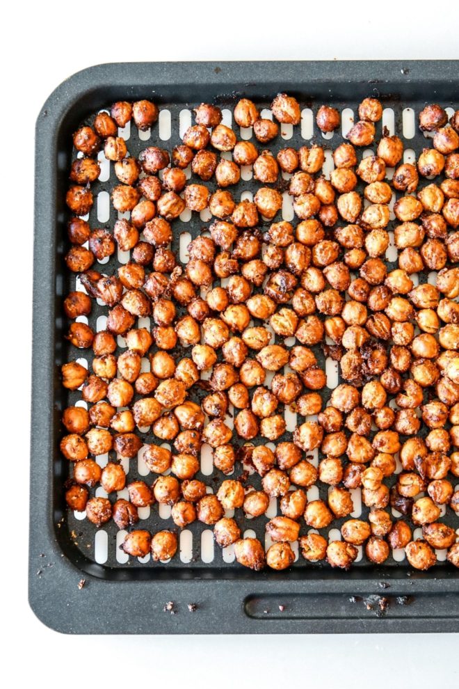 This is an overhead view of an air fryer tray with crispy air fried chickpeas coated with spices. The tray sits on a white counter.
