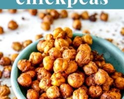 This is a side view of a small turquoise bowl filled with crispy chickpeas. The bowl sits on a white counter with more chickpeas scattered around the bowl. Text overlay reads "crispy crunchy air fryer chickpeas."