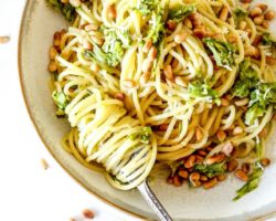 This is an overhead view of a shallow bowl with spaghetti topped with shredded asparagus and toasted pine nuts. A fork has spaghetti twirled around the fork and leaning against the side of the bowl.