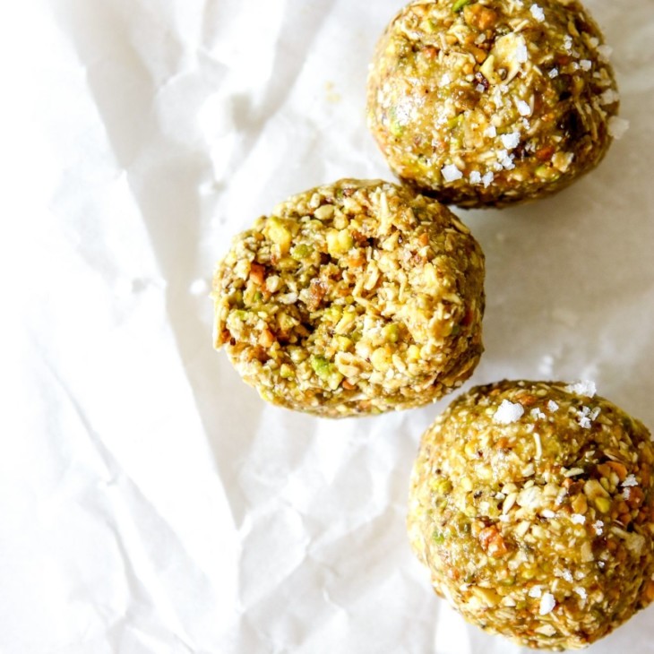 This is an overhead image of pistachio energy balls on a white piece of parchment paper. One energy ball has a bite taken out of it.