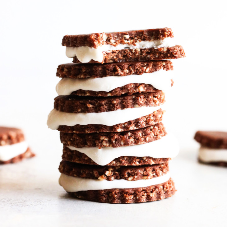 This is a side view of a stack of homemade chocolate sandwich cookies. The cookie sandwiches have a vanilla icing inside. The top cookie has a bite taken out. More cookies are blurred in the background.