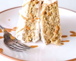 This is a side view of a plate with a slice of banana oat flour cake. The cake has peanut butter frosting. The plate sits on a white counter with a bite background.