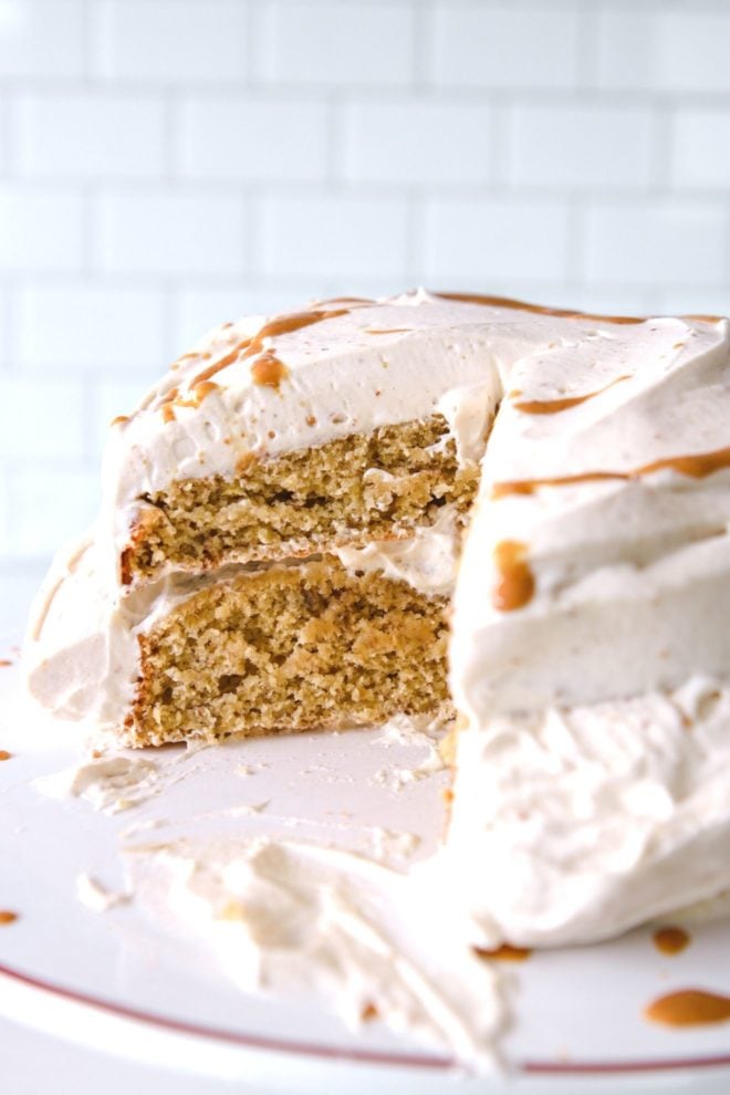 This is a side view of a banana cake with a slice cut out of it revealing the inside two layers of cake with peanut butter whipped frosting on top and in between the layers.