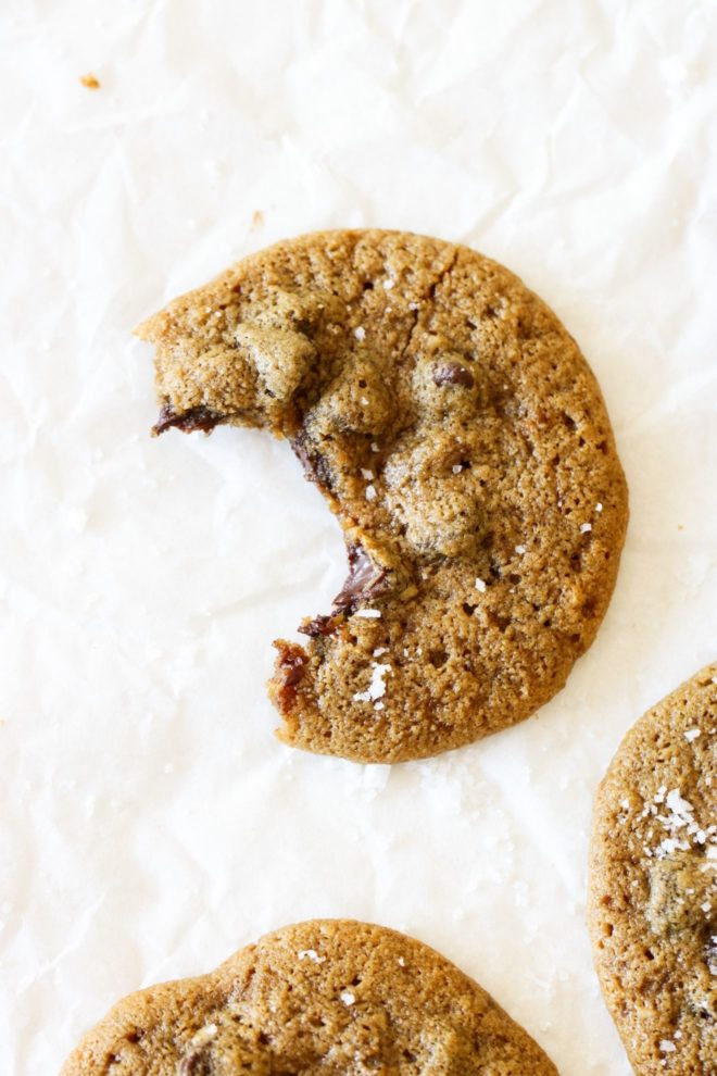 This is an overhead image of an oat flour cookie with chocolate chips and a bite taken out of it. The cookie sits on a white piece of parchment paper.