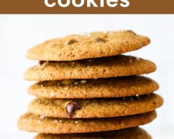 This is a side view of a stack of oat flour chocolate chip cookies. The stack of cookies sits on a white surface with a white background and some blurred cookies in the background. Text overlay reads "oat flour chocolate chip cookies."