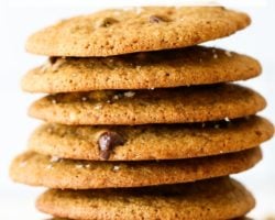 This is a side view of a stack of oat flour chocolate chip cookies. The stack of cookies sits on a white surface with a white background and some blurred cookies in the background. Text overlay reads "oat flour chocolate chip cookies."