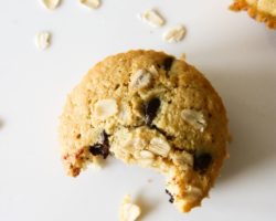 This is an overhead image of an oatmeal chocolate chip muffin with a bite taken out of it. The muffin is sitting on a white counter with another muffin in the top right corner and more oats scattered around the muffins.