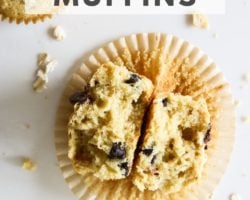 This is an overhead image of an oatmeal chocolate chip muffin broken apart and laying in a muffin wrapper. The wrapper is on the white counter with more oats scattered around it. Text overlay reads "chocolate chip oatmeal muffins."