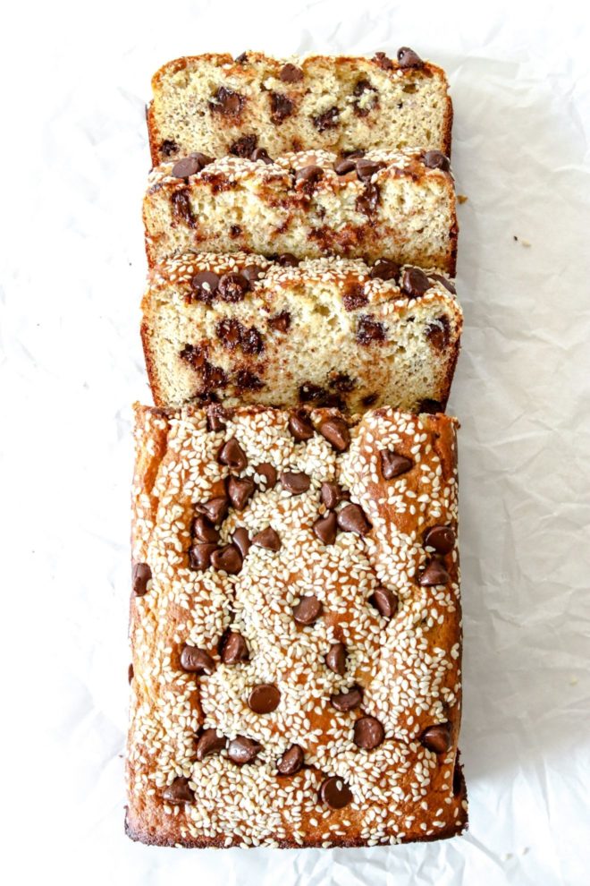 This is an overhead image of a chocolate chip tahini banana bread. Three slices are cut from the bread and are laying down on a white surface.