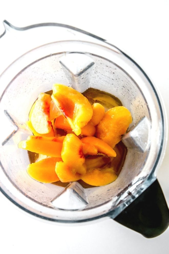 This is an overhead image of a blender with frozen peaches and rum in it. The blender sits on a white counter.