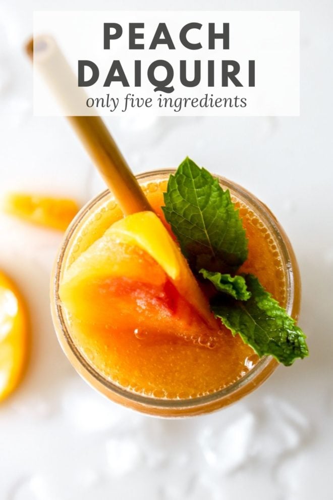 This is an overhead image of a glass filled with Peach Daiquiri. The glass is garnished with peaches and mint leaves. The glass sits on a white counter with ice and peach slices. Text overlay reads "Peach Daiquiris only five ingredients."