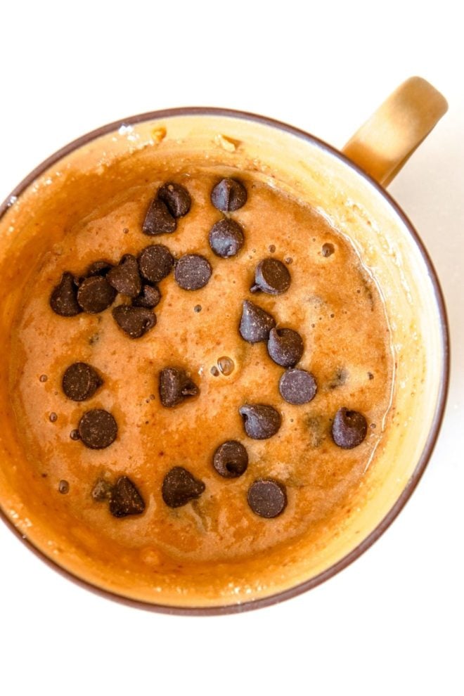 This is an overhead image of a yellow mug with raw banana cake batter topped with chocolate chips. The mug sits on a white counter.