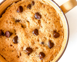 This is an overhead image of a yellow mug with fluffy banana cake with chocolate chips. The mug sits on a white counter with a couple chocolate chips on the counter.