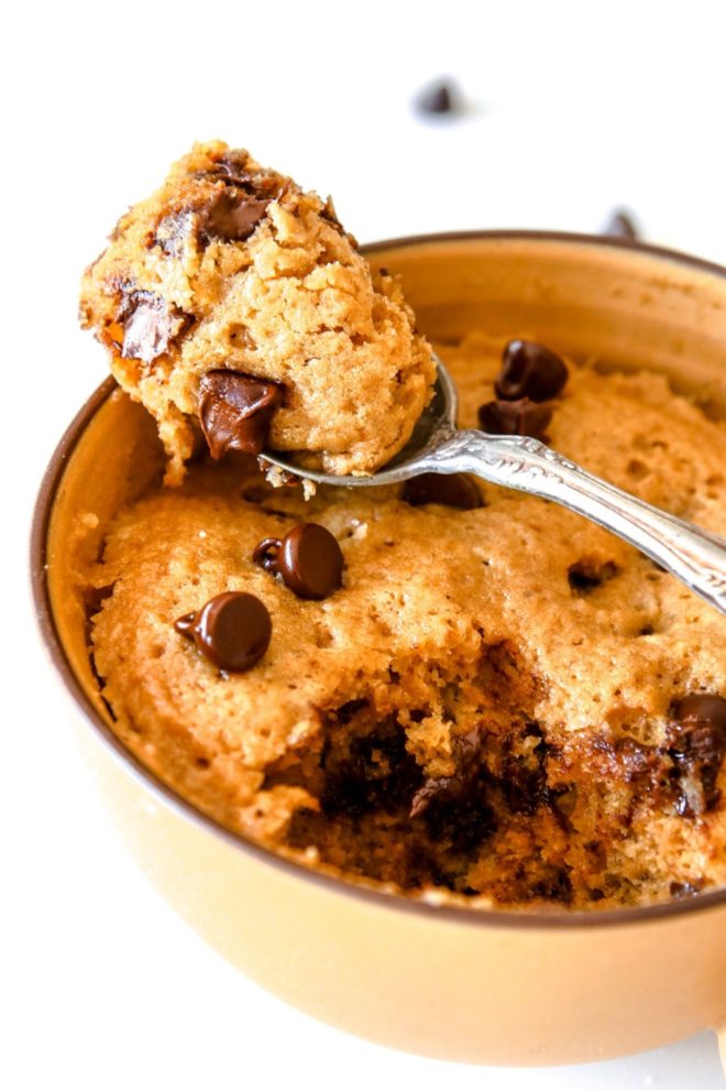 This is a side image of fluffy cake in a yellow mug. A spoon is scooping out a bite of cake and leaning against the mug.