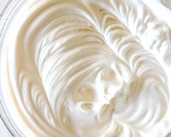 This is an overhead image of a glass bowl on a white surface. Inside the bowl is fluffy white meringue.