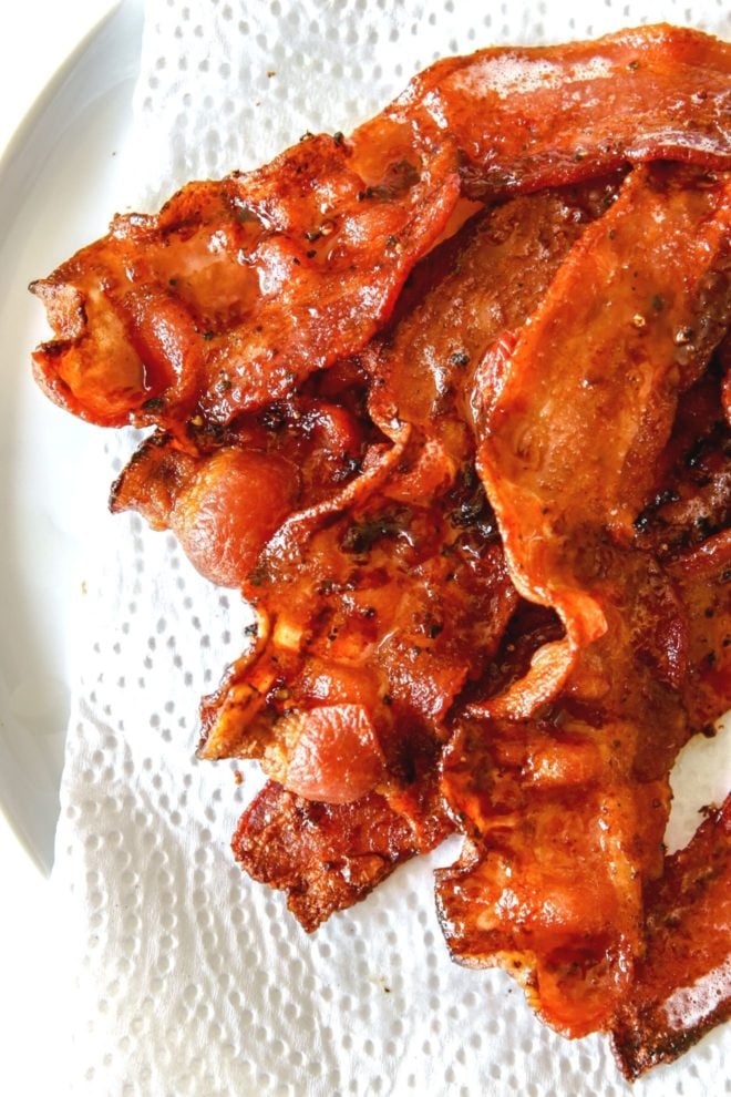This is an overhead image of crispy bacon slices on a plate lined with a paper towel.