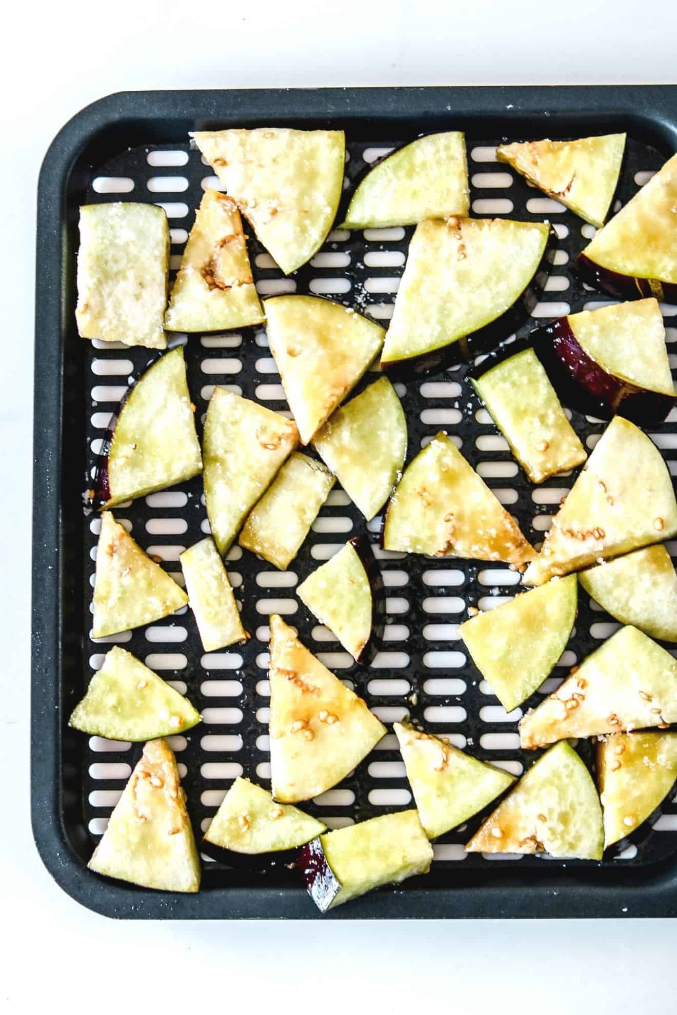 This is an overhead image of an air fryer tray with raw eggplant pieces on it. The eggplant is sprinkled with salt.