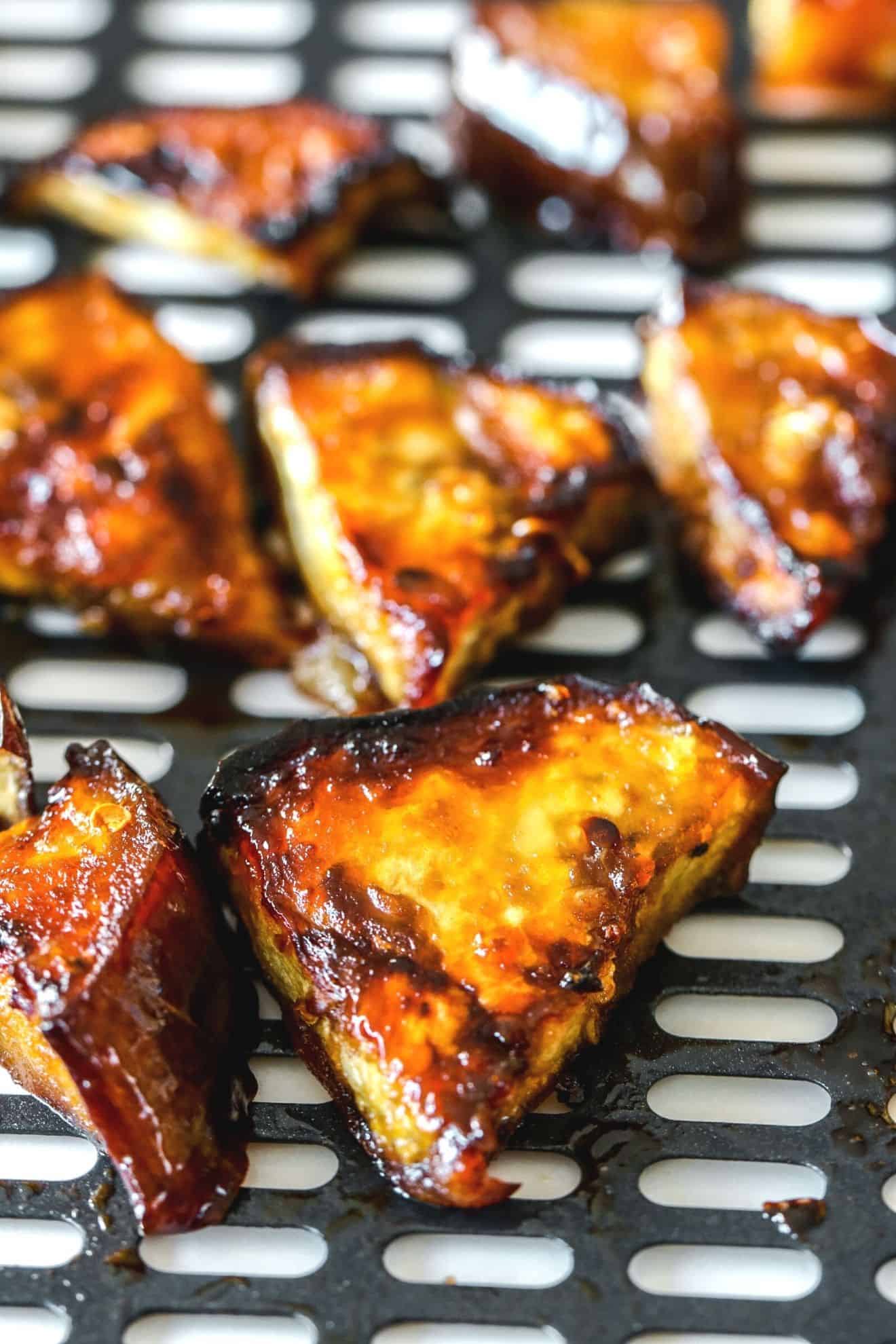 This is a side view of an air fryer tray with caramelized and glazed eggplant pieces.