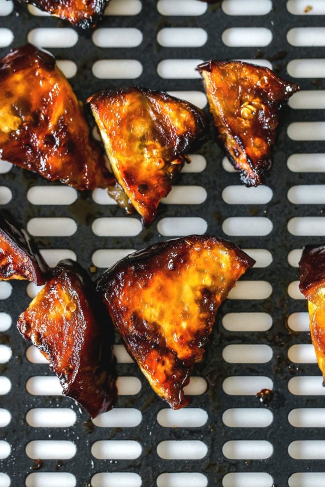 This is an overhead image of an air fryer tray with caramelized and glazed eggplant pieces.