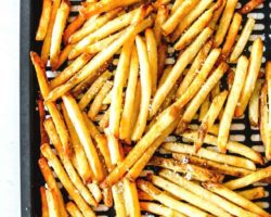 This is an overhead image of an air fryer tray with cooked french fries on it. The fries are sprinkled with salt. The tray is on a white paper towel and on a white counter.