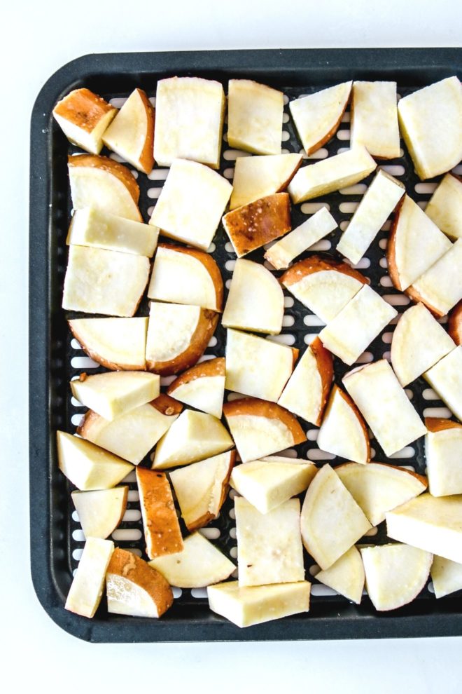 This is an overhead image of an air fryer tray with raw white sweet potato pieces on it. The tray sits on a white background.
