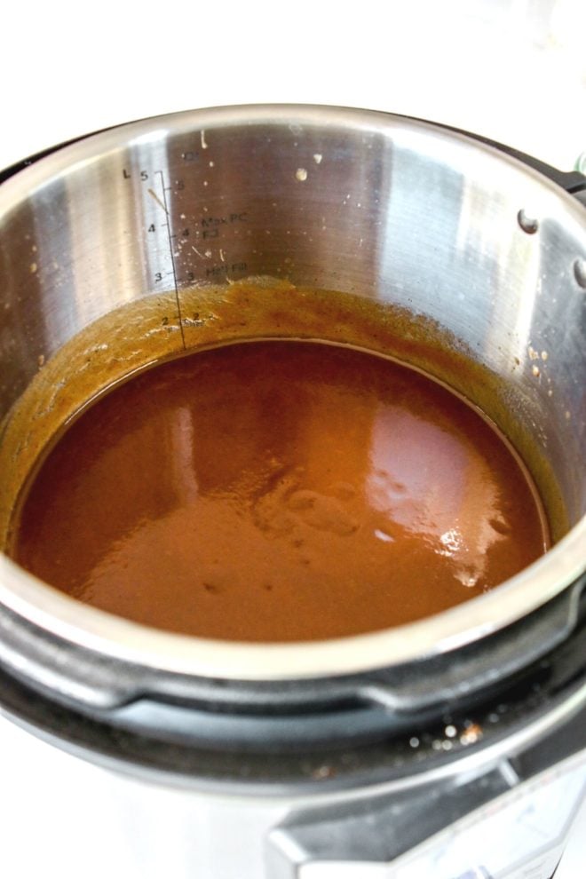 This image is peering into an instant pot with smooth, brown apple butter. The instant pot sits on a white counter.