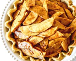 This is an overhead image of an apple pie in a white pie dish with a cooked pie crust and raw apples coated with cinnamon in it.