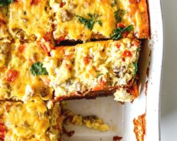 This is an overhead image of a breakfast casserole cut into 8 pieces in the casserole dish. One piece of the casserole is missing and one piece is turned on the side to show the peppers, onions, and sausage pieces in the casserole.