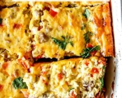 This is an overhead image of a breakfast casserole cut into 8 pieces in the casserole dish. One piece of the casserole is missing and one piece is turned on the side to show the peppers, onions, and sausage pieces in the casserole. Text overlay reads "keto breakfast casserole."