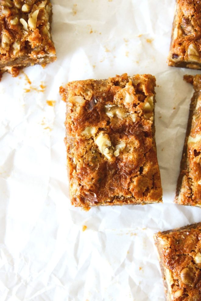 This is an overhead image of butterscotch blondies with walnuts. The blondie sits on a white piece of parchment paper with more blondies on the sides of the image.