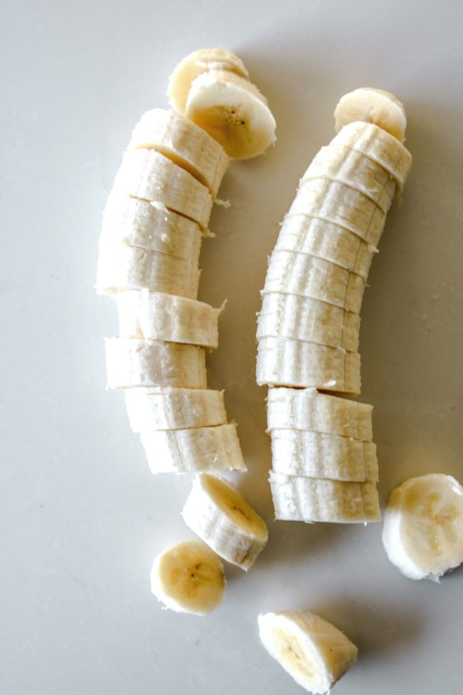 This is an overhead image of two bananas sitting on a white counter. The bananas are cut into 1/2 inch rounds.