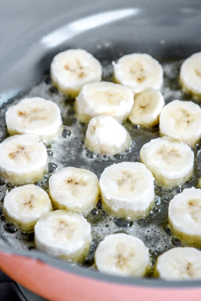 This is a side view looking into a pan with bananas frying in butter. The top of the bananas are raw and haven't been sautéd yet.