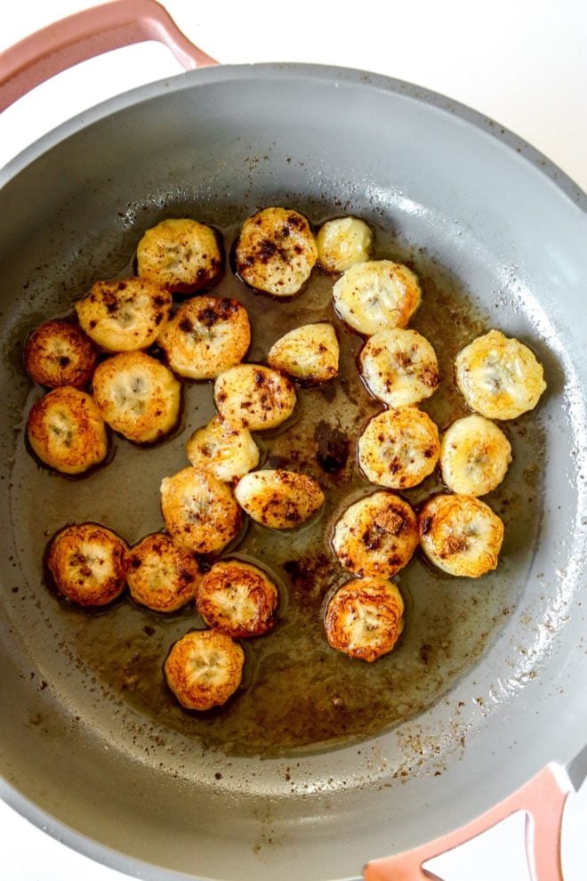 This is an overhead view of a pan with caramelized bananas in it. The bananas are sprinkled with cinnamon. The pan sits on a white counter.