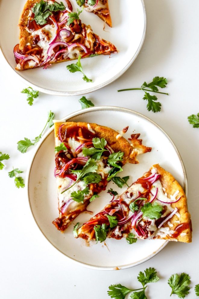 This is an overhead image of two white plates with two pieces of pizza on each plate. The pizza is topped with bbq sauce, red onions, and cilantro. The plates sit on a white counter.