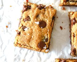 This is an overhead image of blondies on a white piece of parchment paper. The image focuses on one blondie in the middle and more blondies are seen to the top and right and bottom of the image.