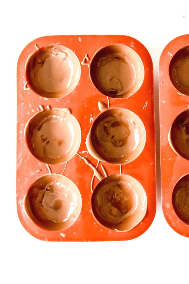 This is an overhead image of red silicone semi-sphere molds filled with melted chocolate. The molds sit on a white surface.
