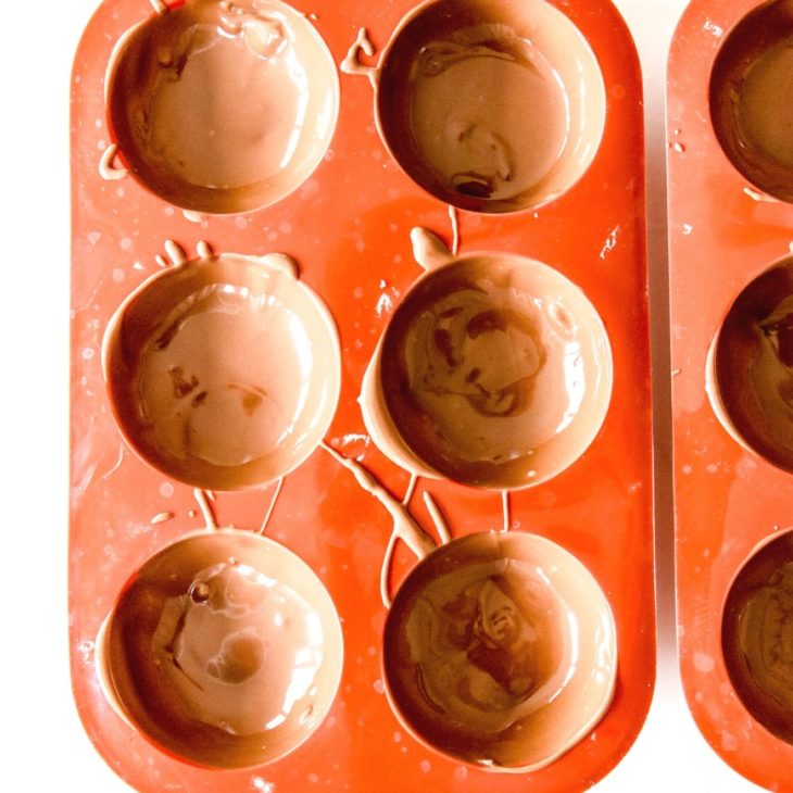 This is an overhead image of red silicone semi-sphere molds filled with melted chocolate. The molds sit on a white surface.