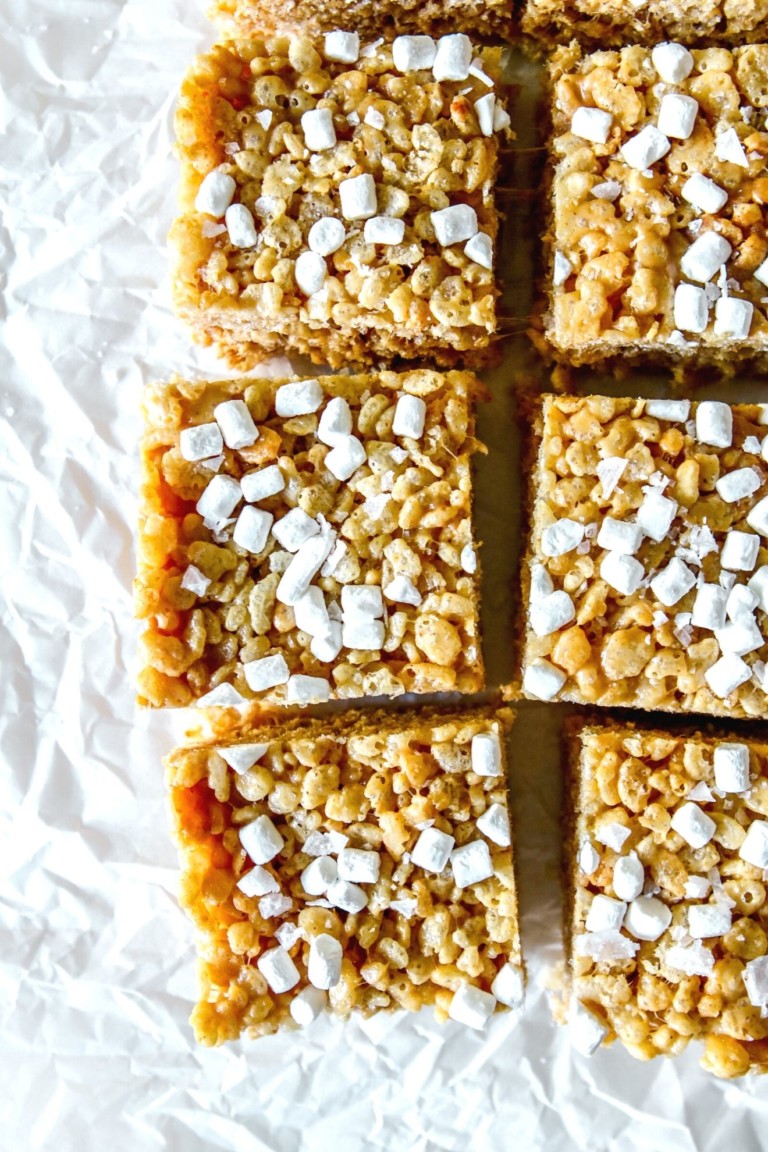 This is an overhead image of peanut butter rice krispie treats cut into squares and topped with mini marshmallows. The treats sit on a white piece of crumpled parchment paper.