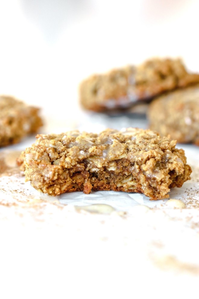 This is a side view of a pumpkin oatmeal cookie with a bite taken out of it. The cookie sits on a white surface with more cookies blurred in the background.