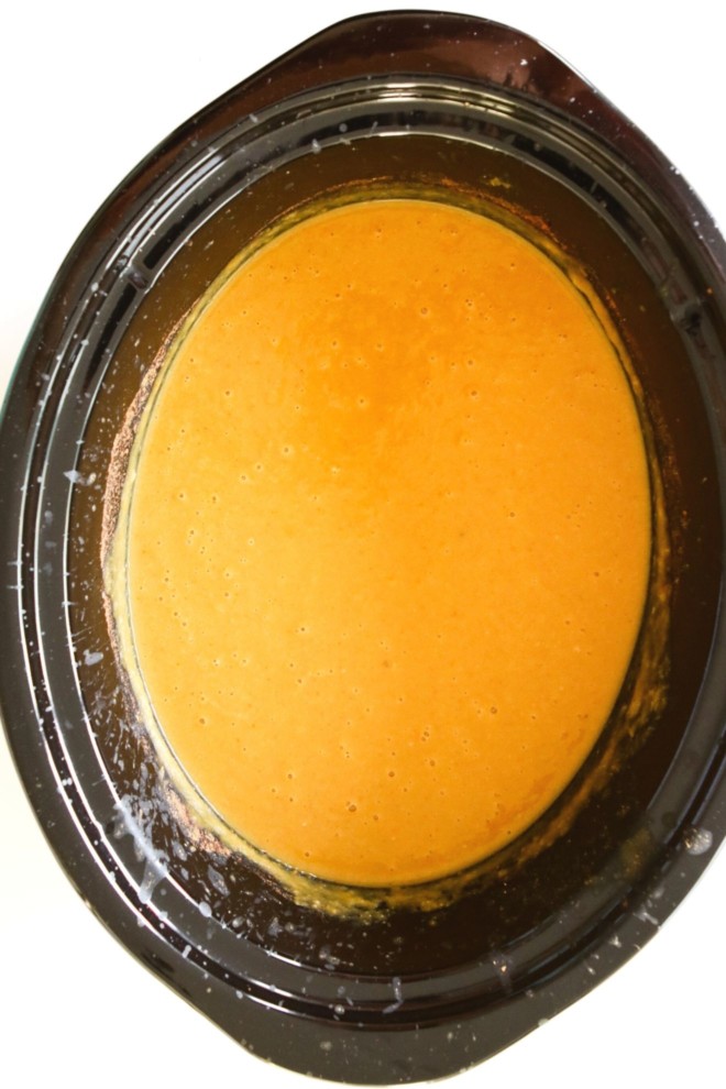 This is an overhead image of a slow cooker with blended pumpkin soup inside. The slow cooker sits on a white background.