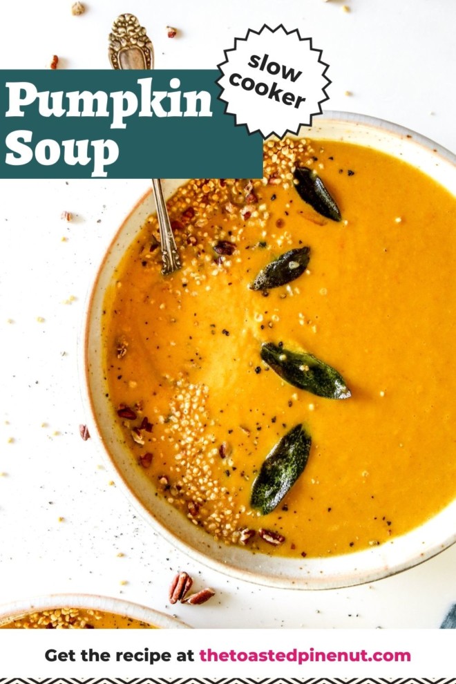 This is an overhead image of a shallow bowl with pumpkin soup on a white counter. The soup is topped with sage leaves, pecans, and quinoa. A spoon is dipping into the soup to the left side of the bowl. Text overlay reads "slow cooker pumpkin soup."