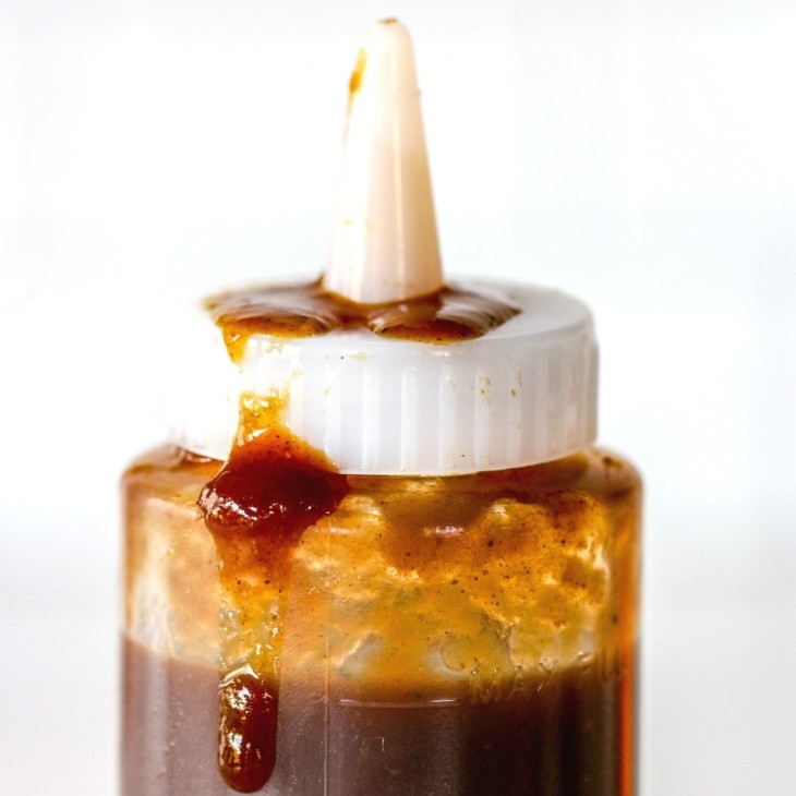 This is a closeup of a plastic squeeze bottle with a lid. Inside the bottle is a deep caramel brown color. Some of the syrup is on the lid and dripping down the side of the bottle.
